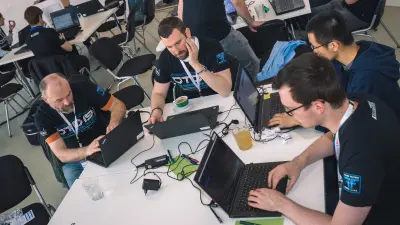Männer sitzen mit ihren Laptops an einem Tisch und programmieren.